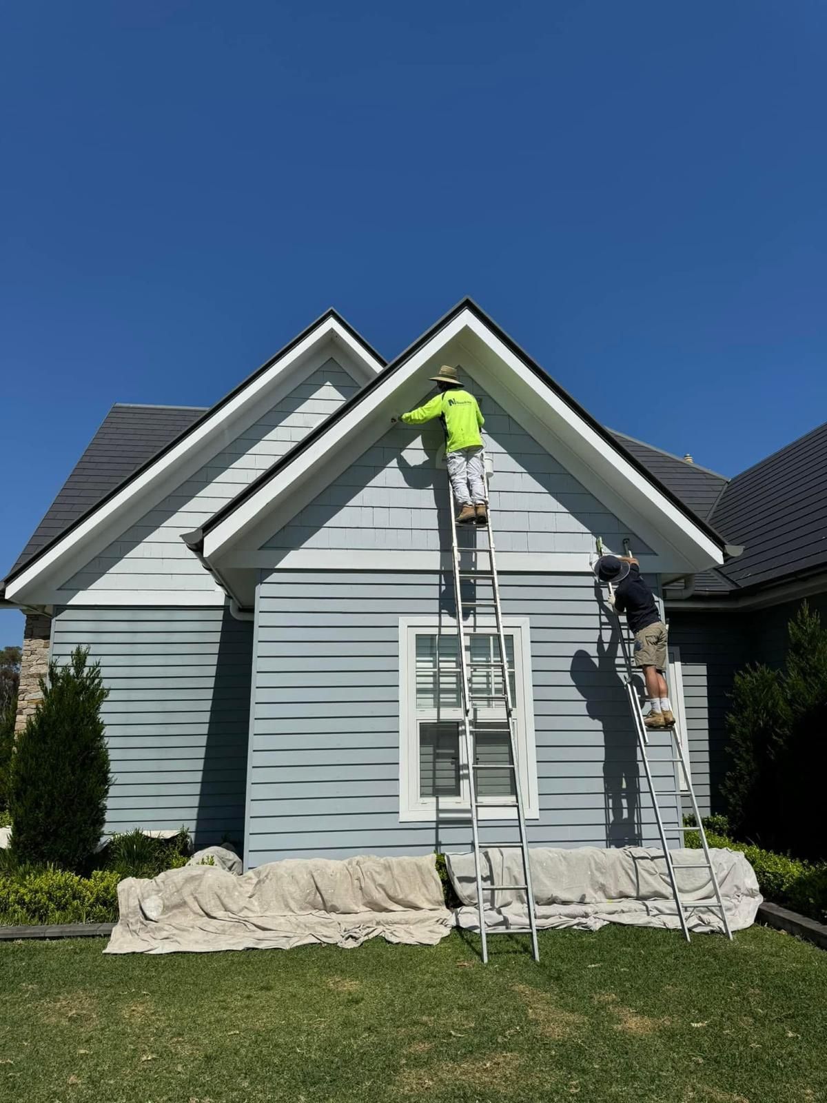 A man on a ladder is painting the side of a house.