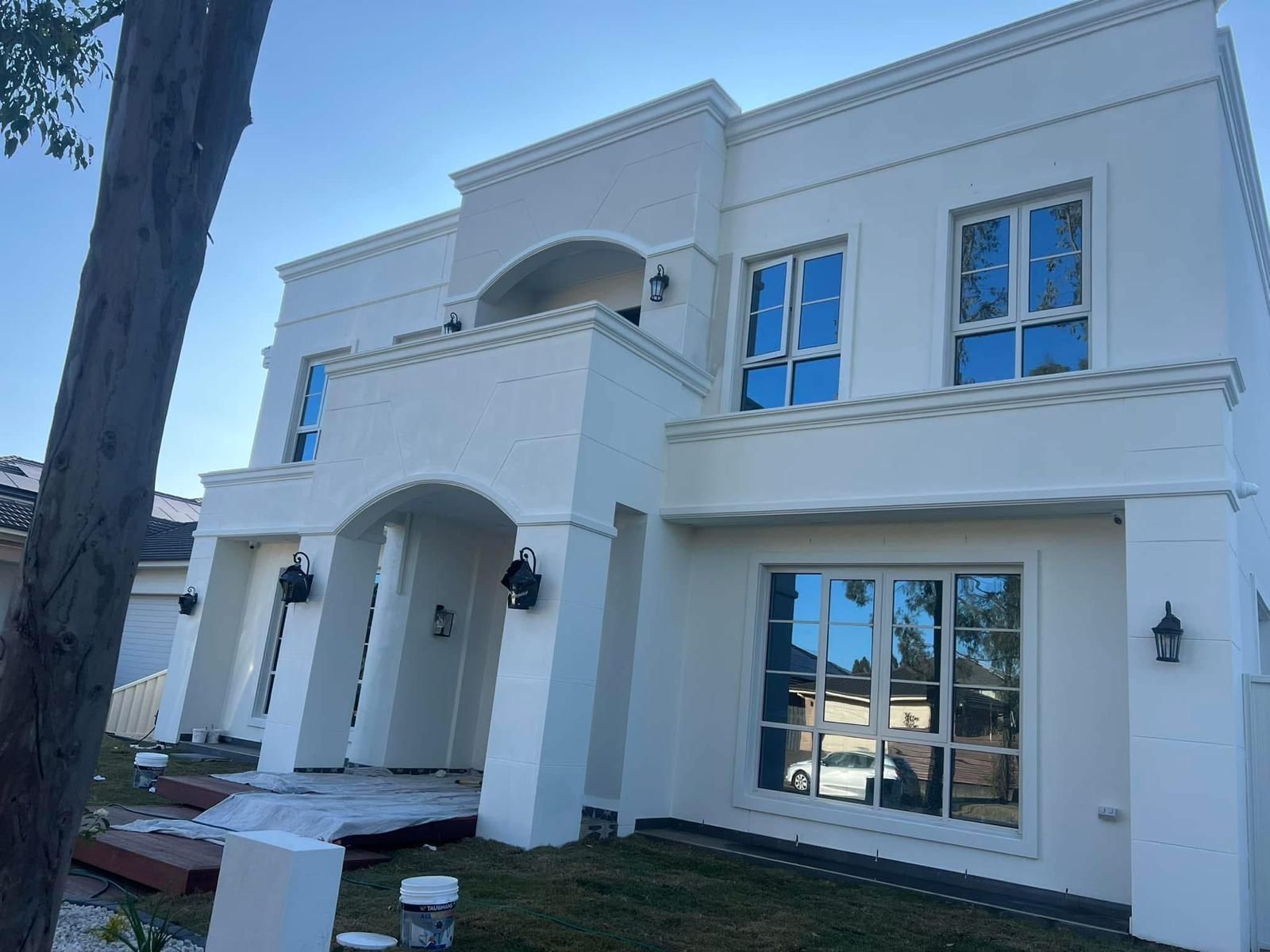 A large white house with blue windows is being painted.