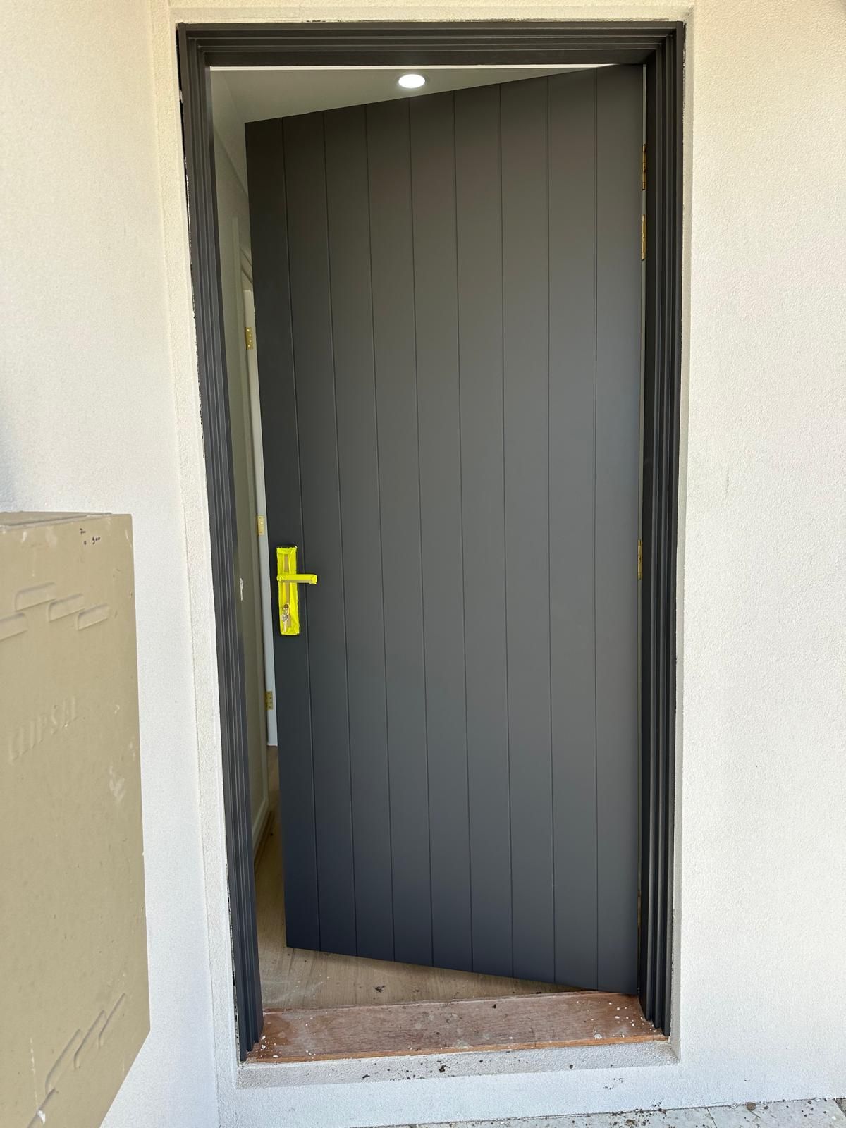 A black door with a yellow handle is open on a white wall.