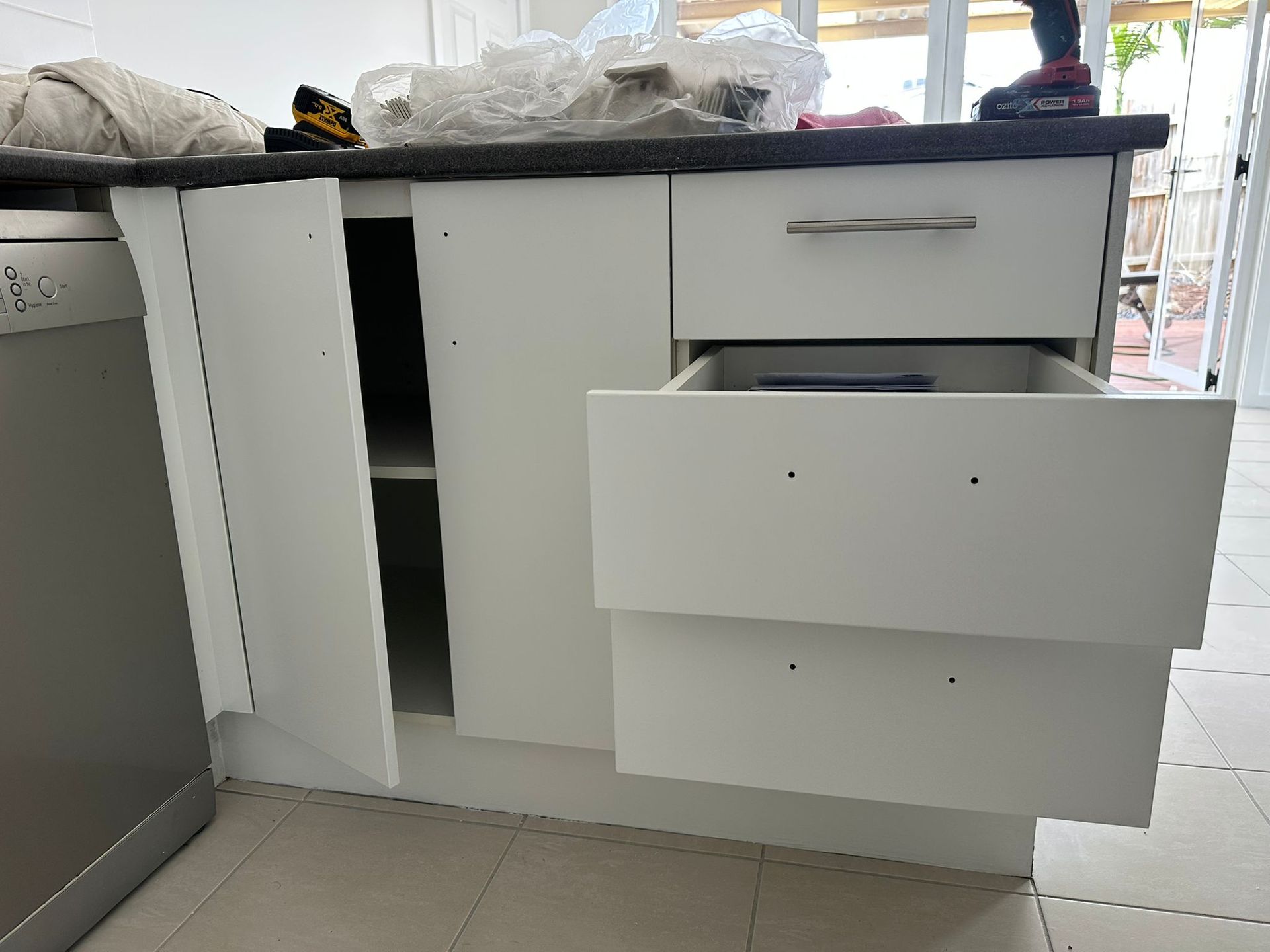 A kitchen cabinet with a drawer open and a dishwasher in the background.