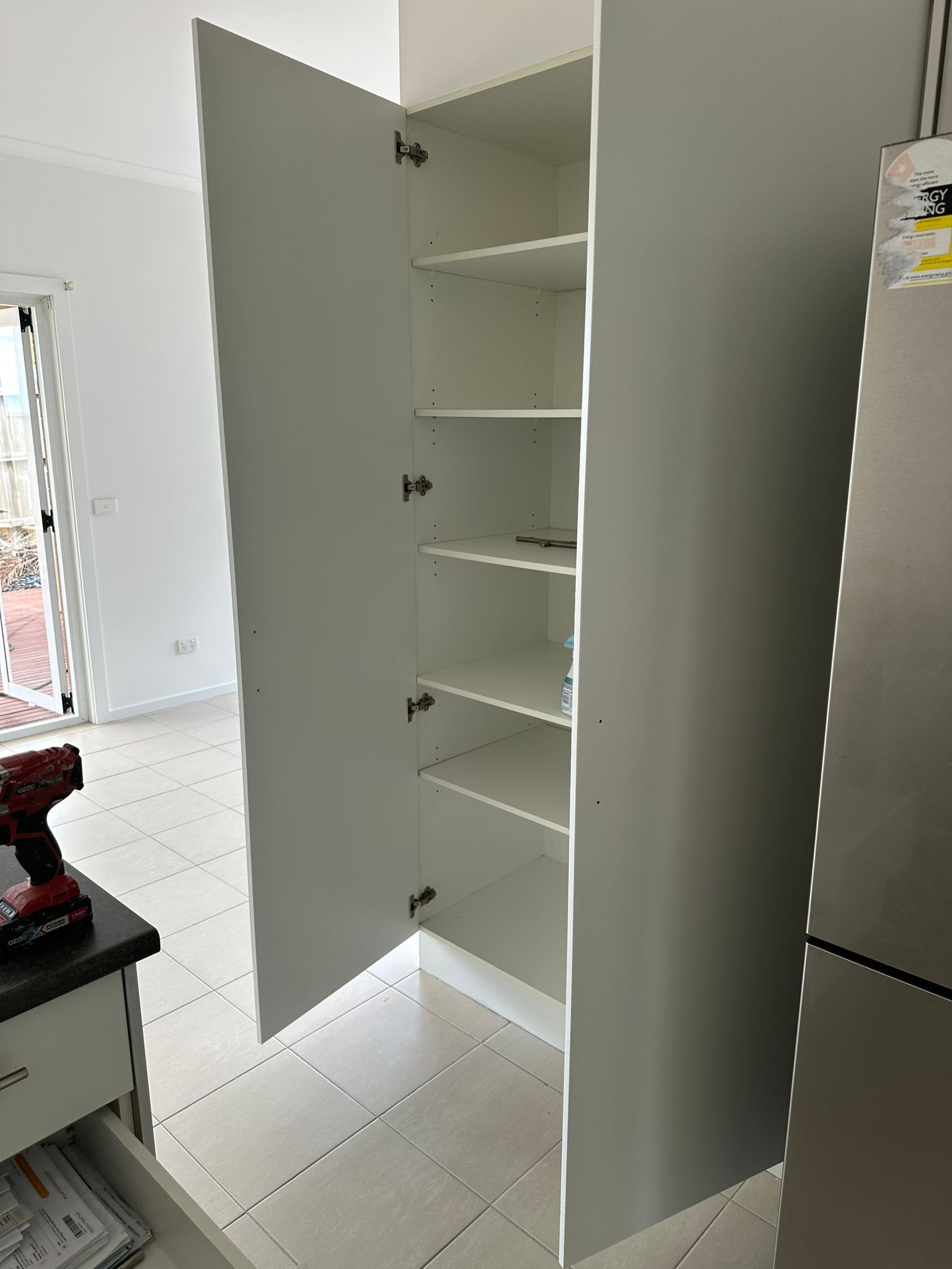 A white cabinet with the door open in a kitchen next to a refrigerator.