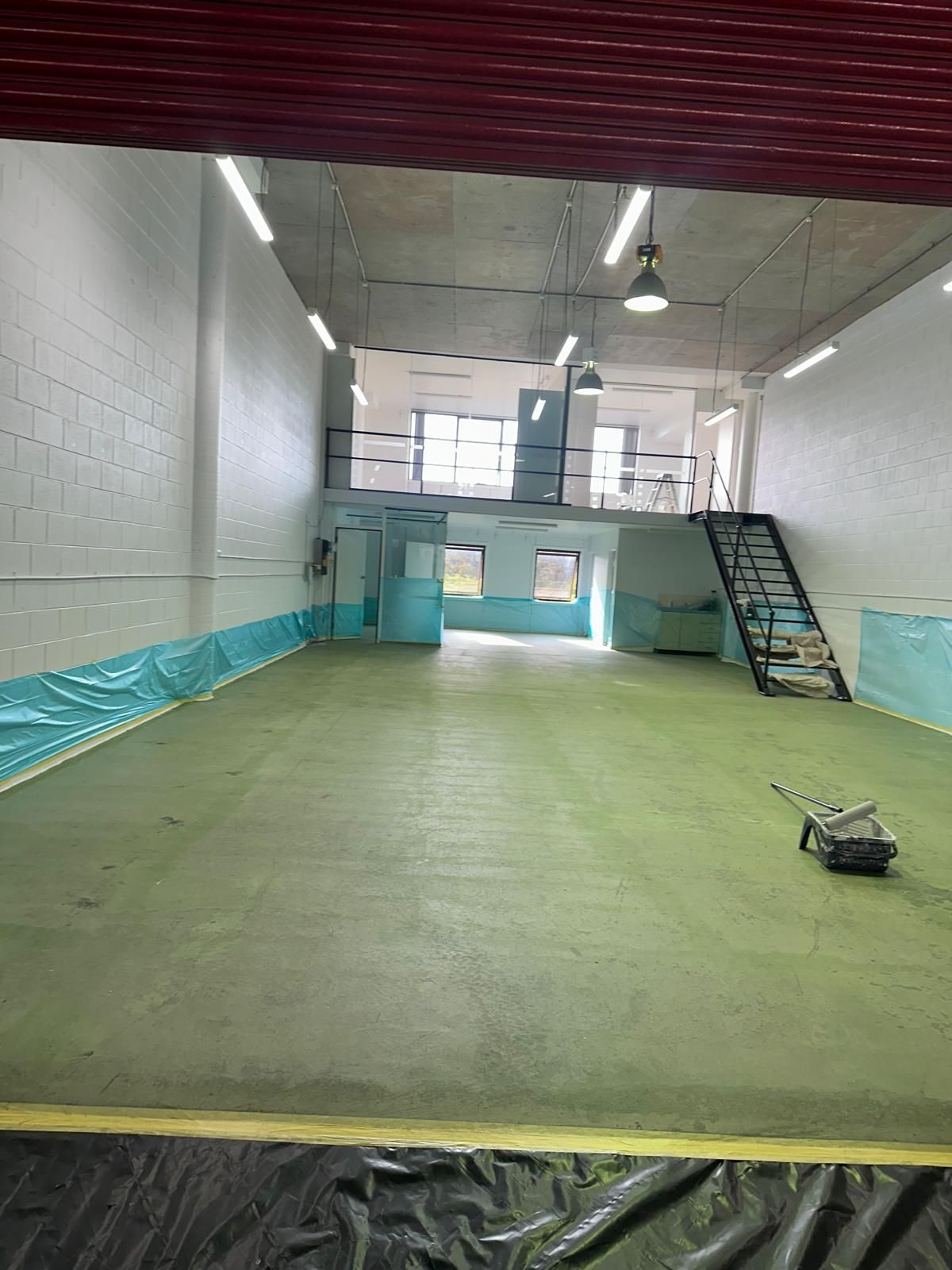 A large empty warehouse with a green floor and stairs.