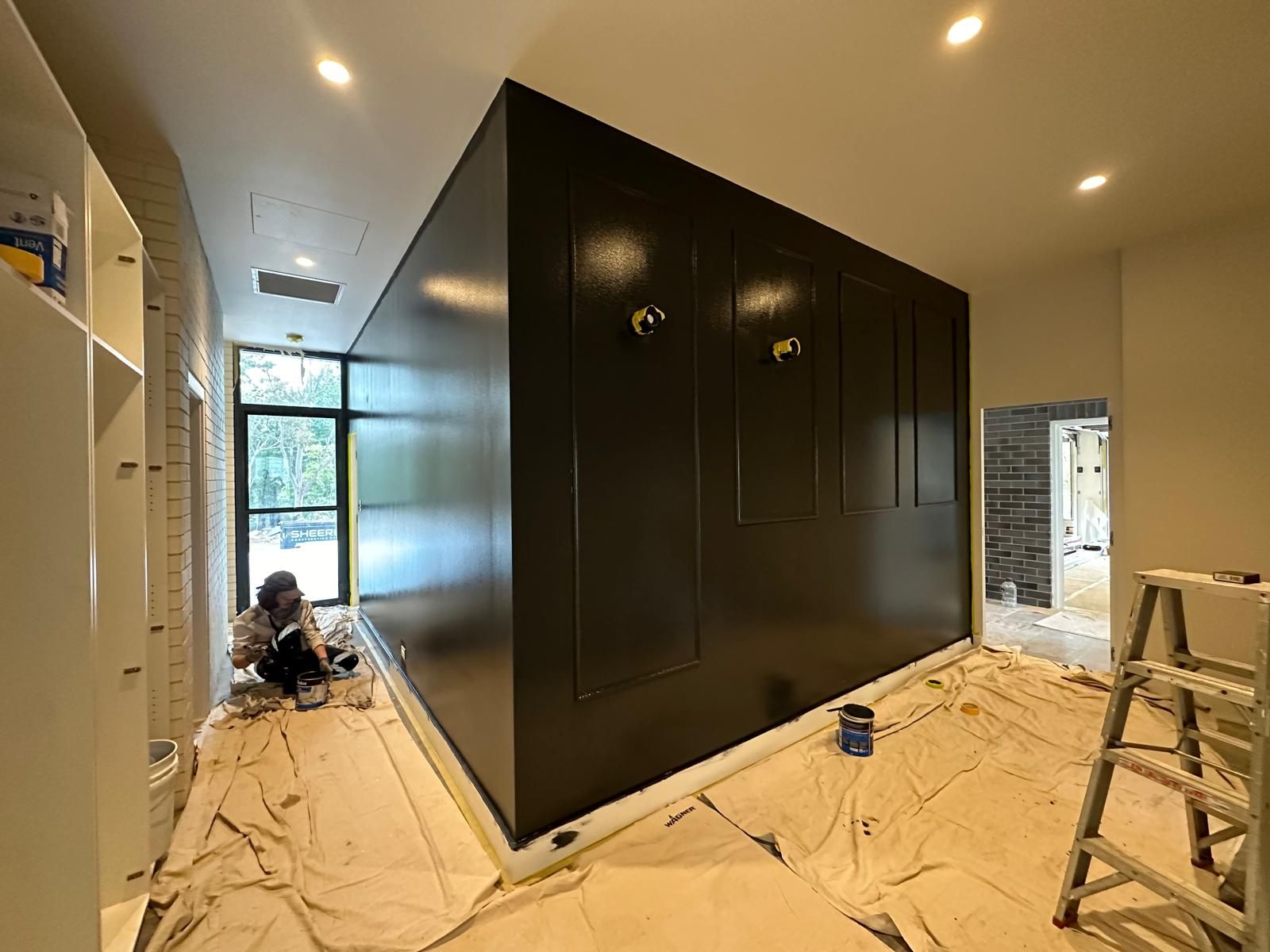 A person is sitting on the floor in a room painting a wall.
