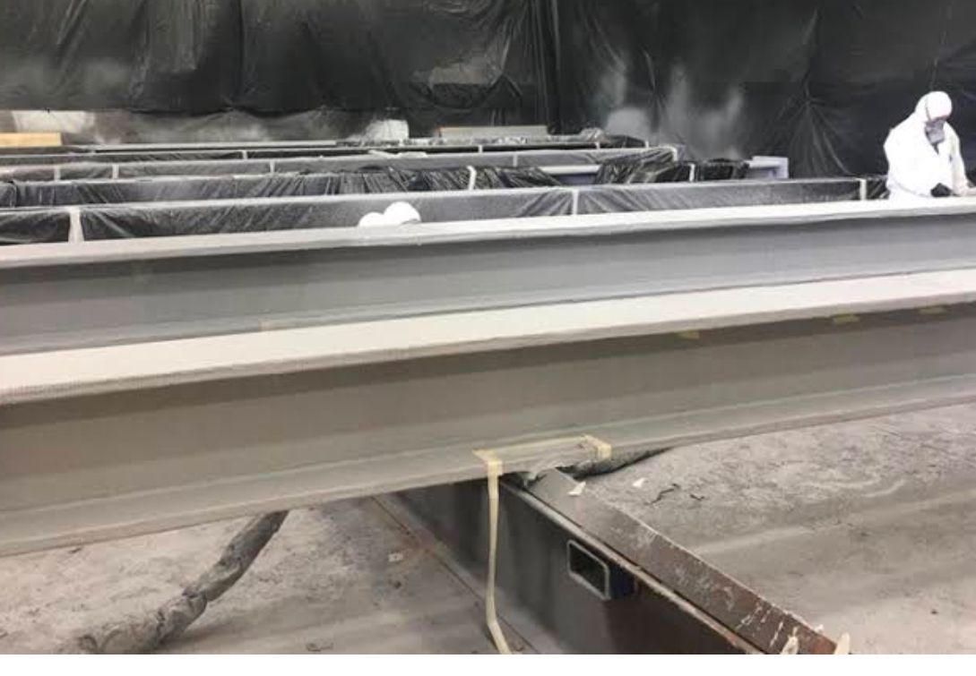 A metal structure is being painted in a factory.