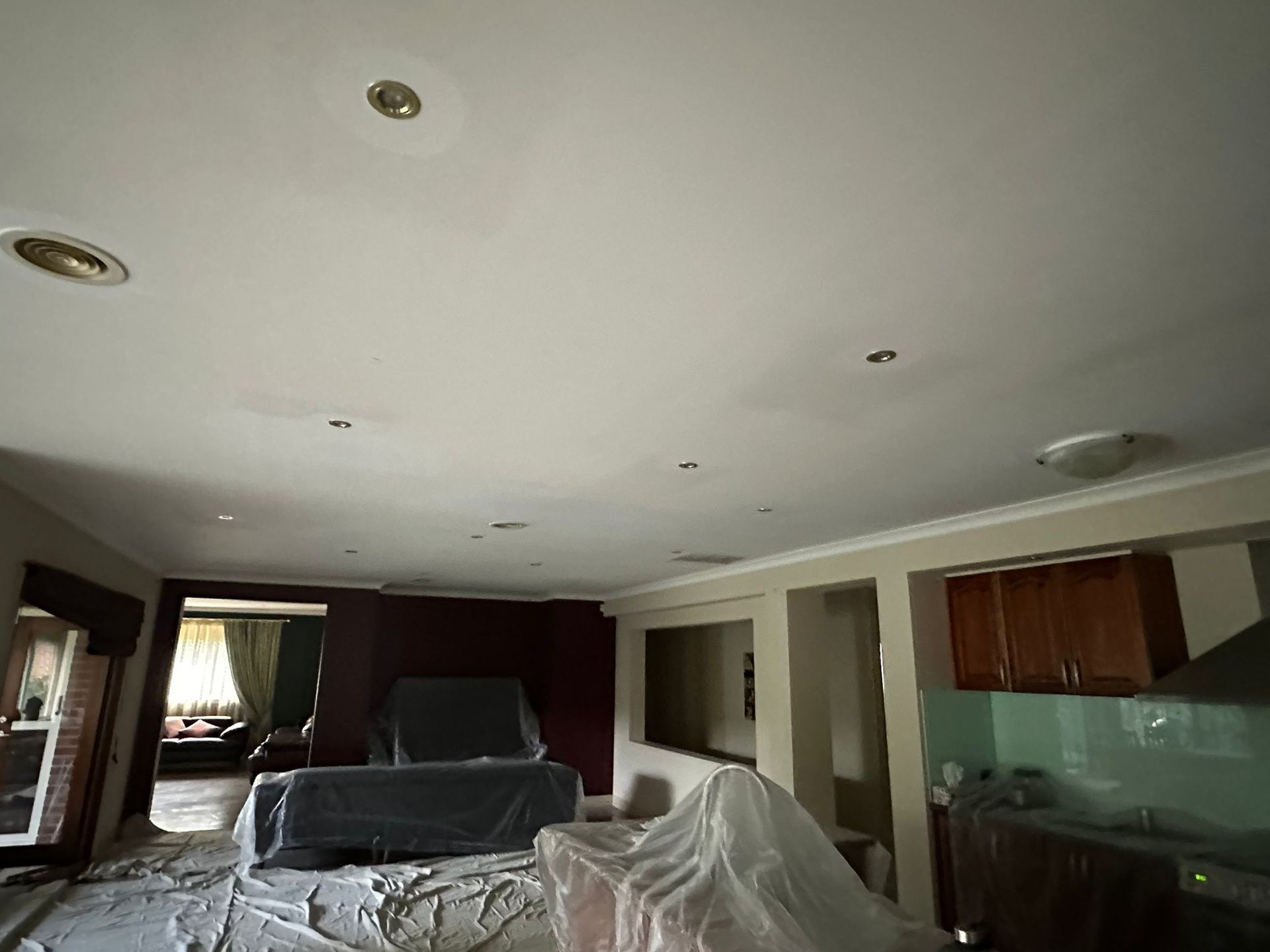 A living room with a white ceiling and a couch covered in plastic.