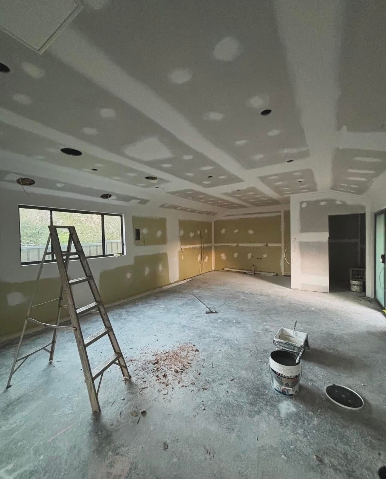 An empty room with a ladder and buckets of paint