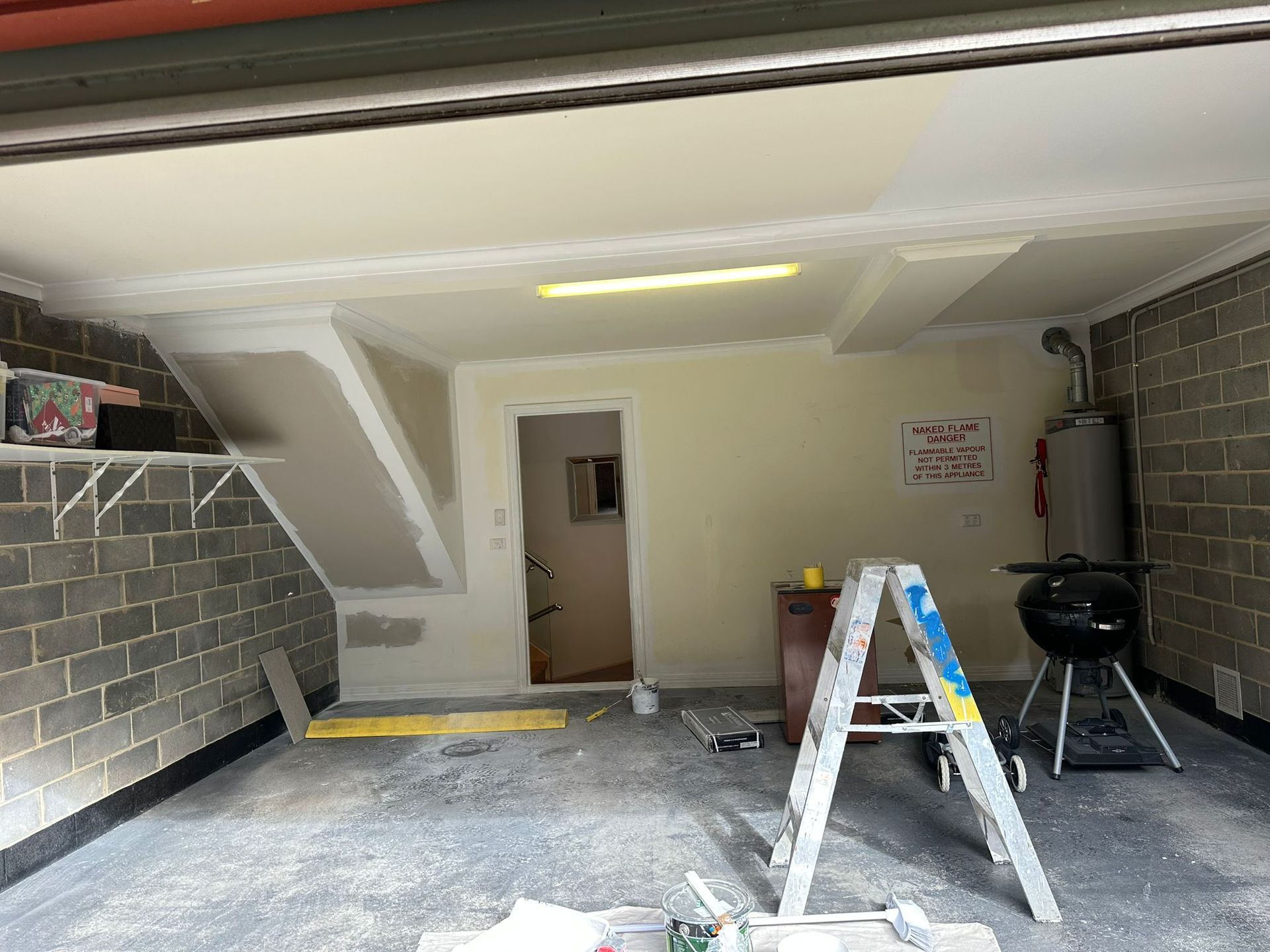 A garage is being painted with a ladder in the middle of the room.