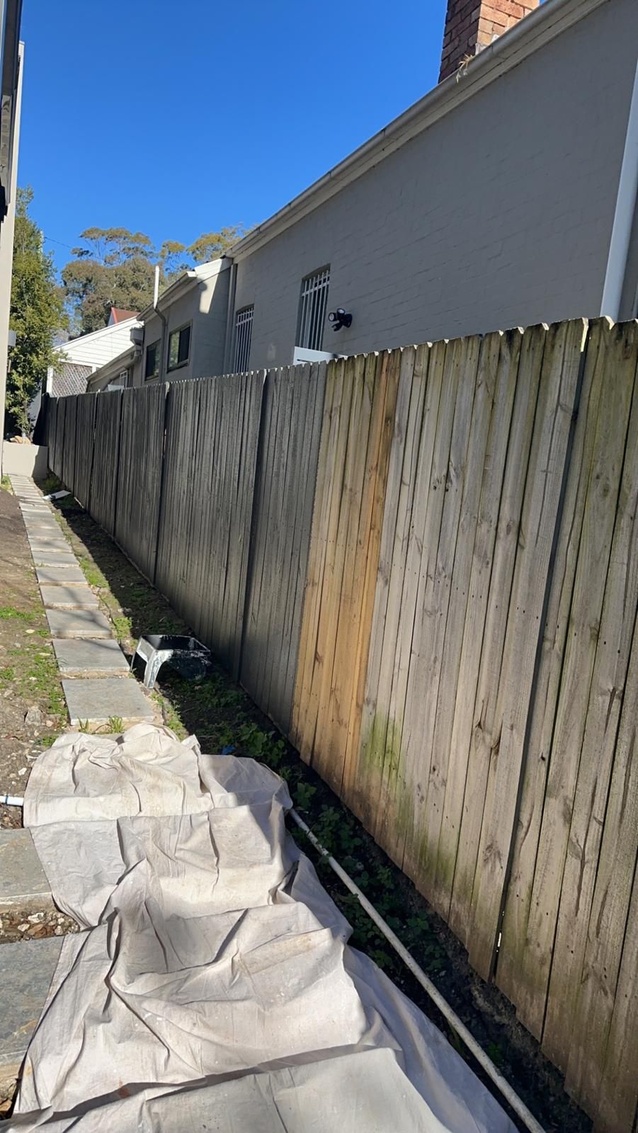 A wooden fence is sitting next to a sidewalk next to a building.