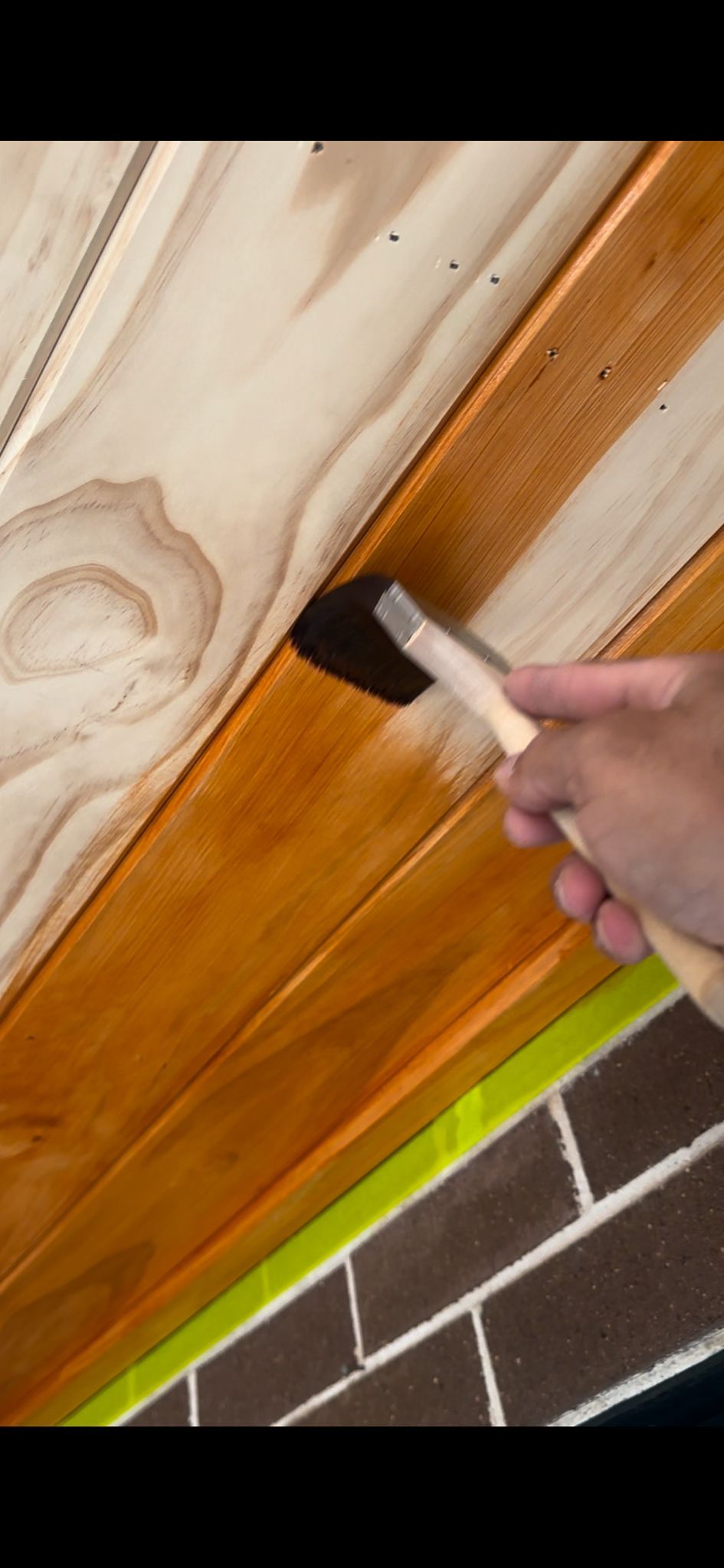 A person is painting a wooden ceiling with a brush.