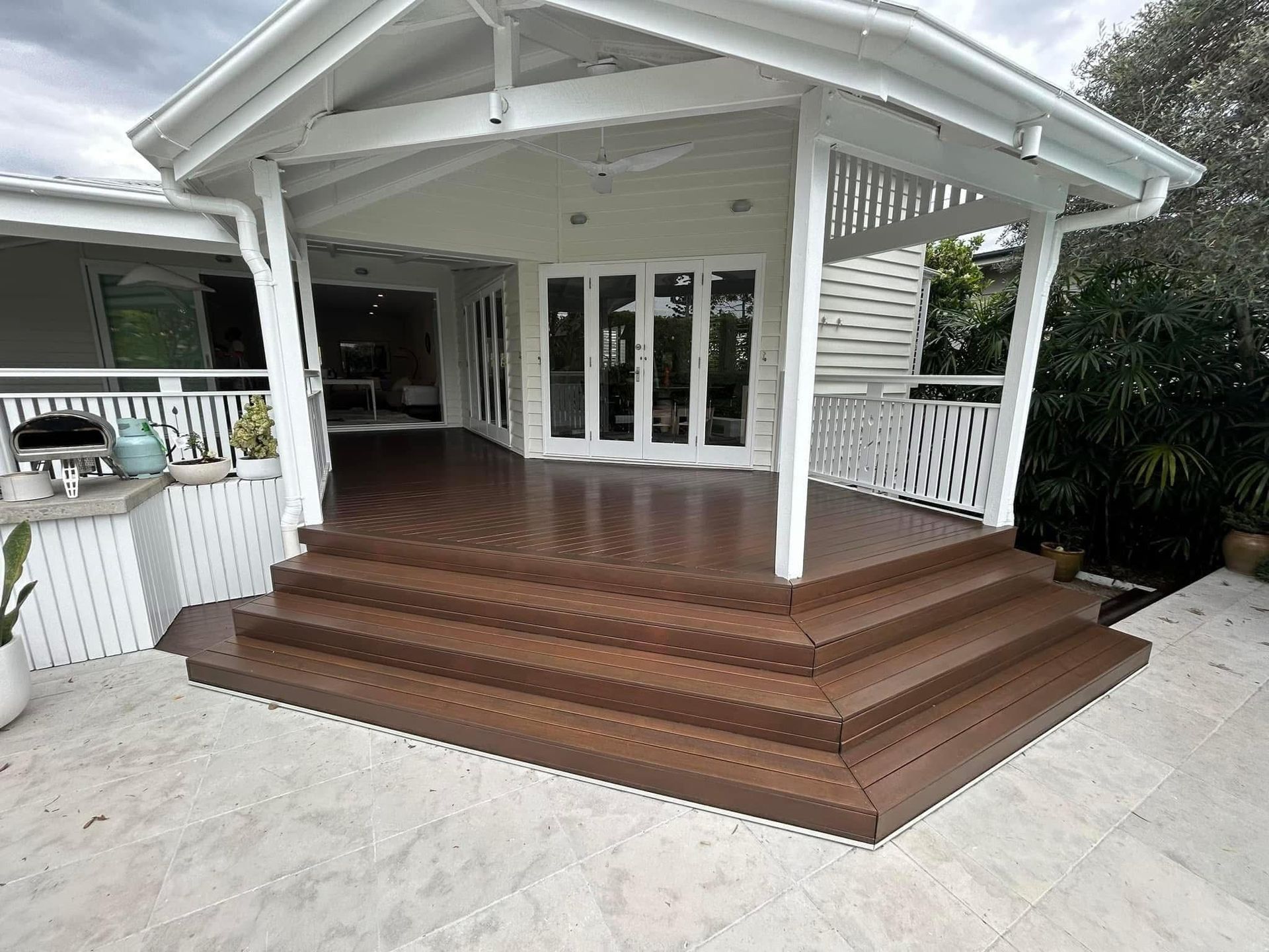 A white house with a wooden deck and stairs leading up to it.