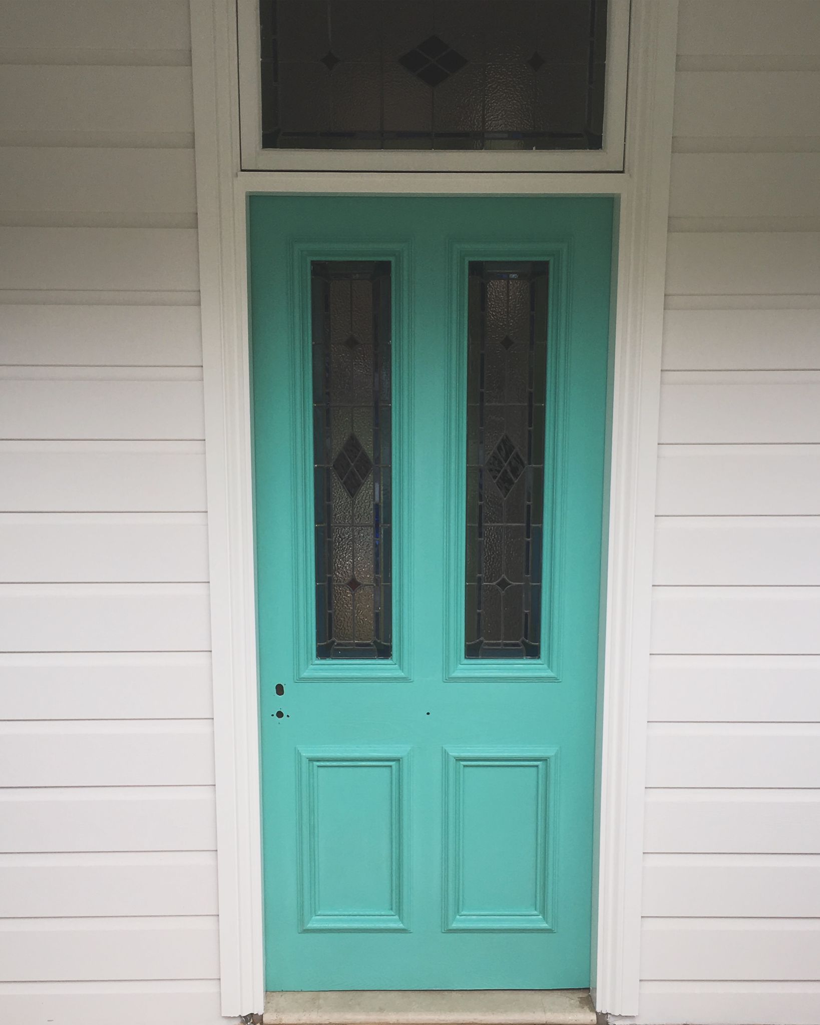 A turquoise front door with two windows on a white house.