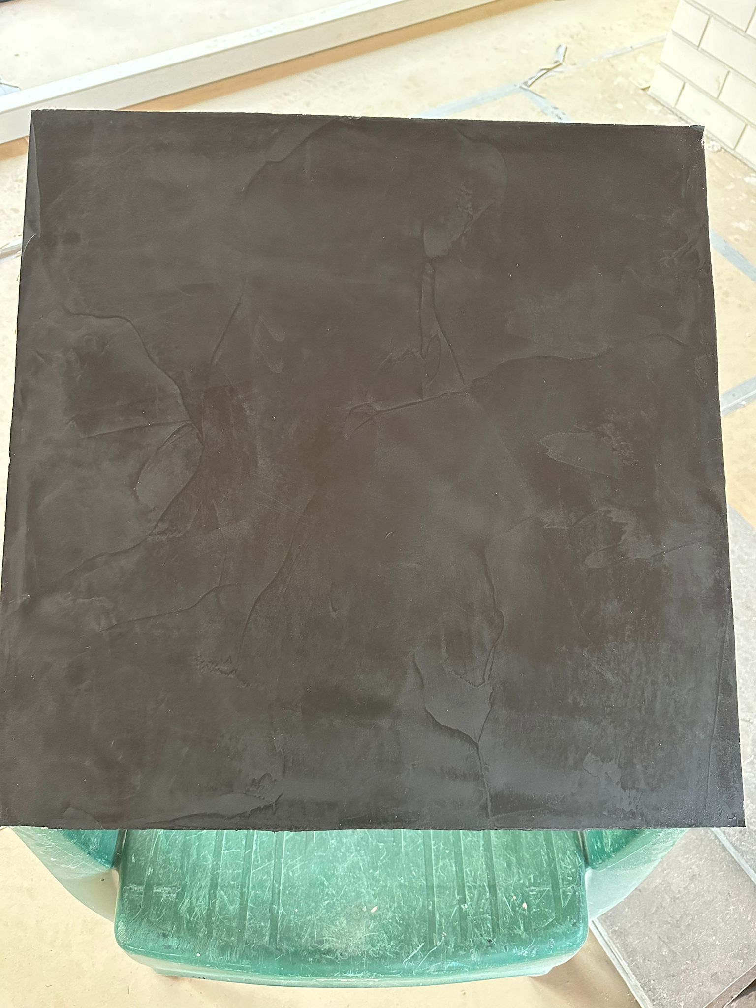 A black square tile is sitting on top of a green chair.