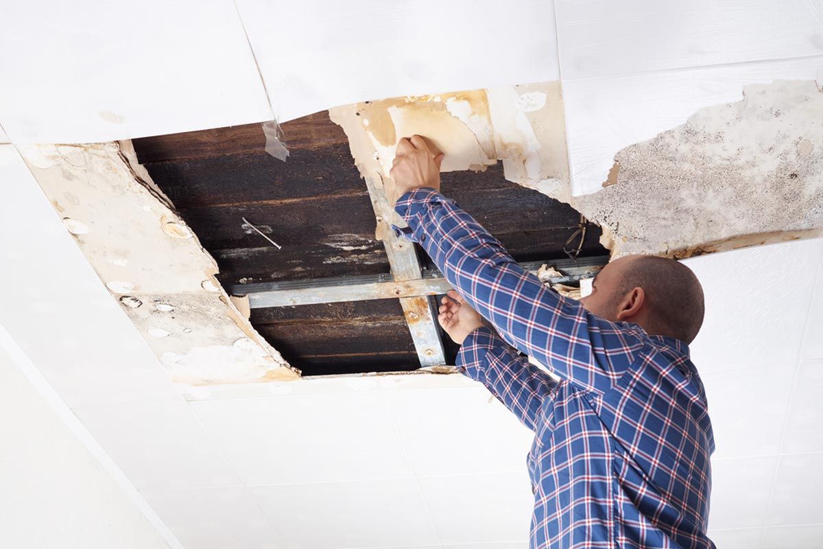 A man in a plaid shirt is working on a ceiling.