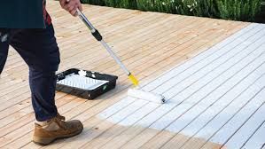 A man is painting a wooden deck with a roller.