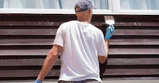 A man is painting a wooden wall with a brush.