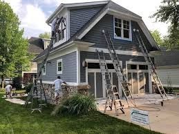 A group of people are painting a house with ladders.