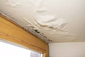 A ceiling with water damage and a window in a room.