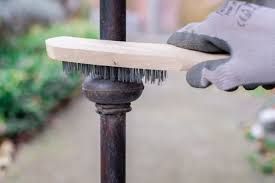 A person is cleaning a metal post with a wire brush.