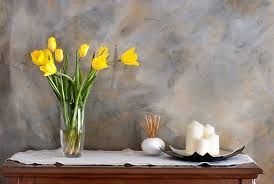A vase of yellow tulips is sitting on a wooden table next to a candle.