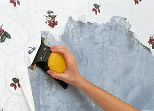 A person is removing wallpaper from a wall with a spatula.