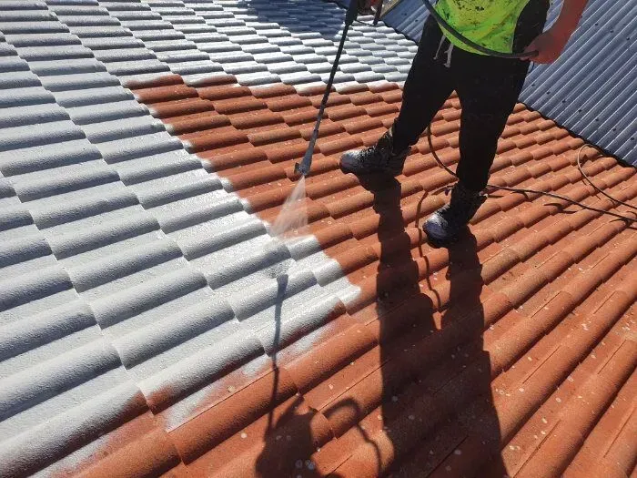 A man is cleaning a tiled roof with a high pressure washer.