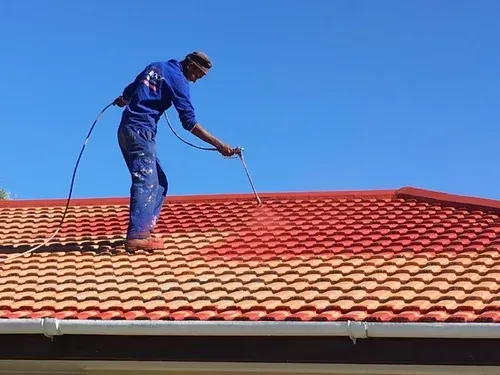 A man is spraying red paint on a tiled roof.