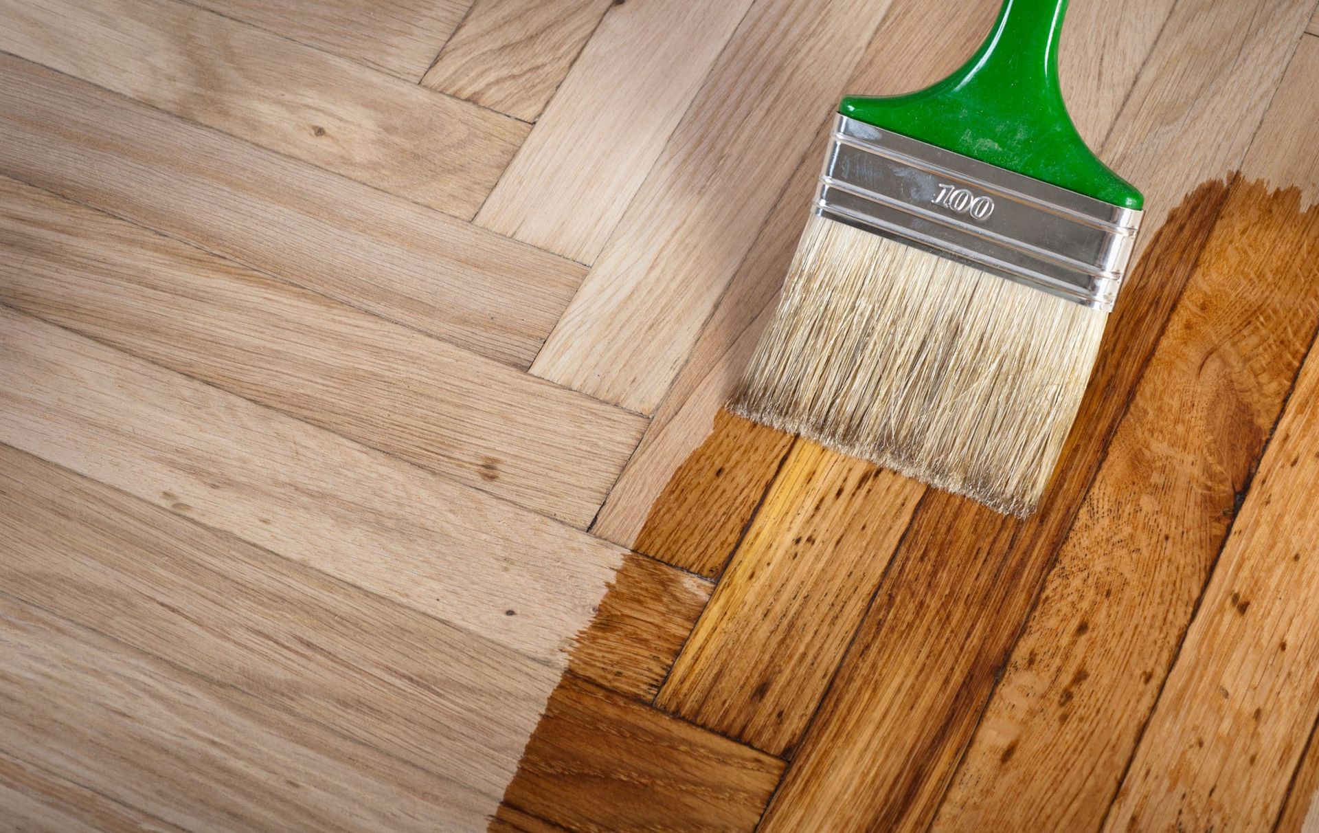 A brush is being used to paint a wooden floor.