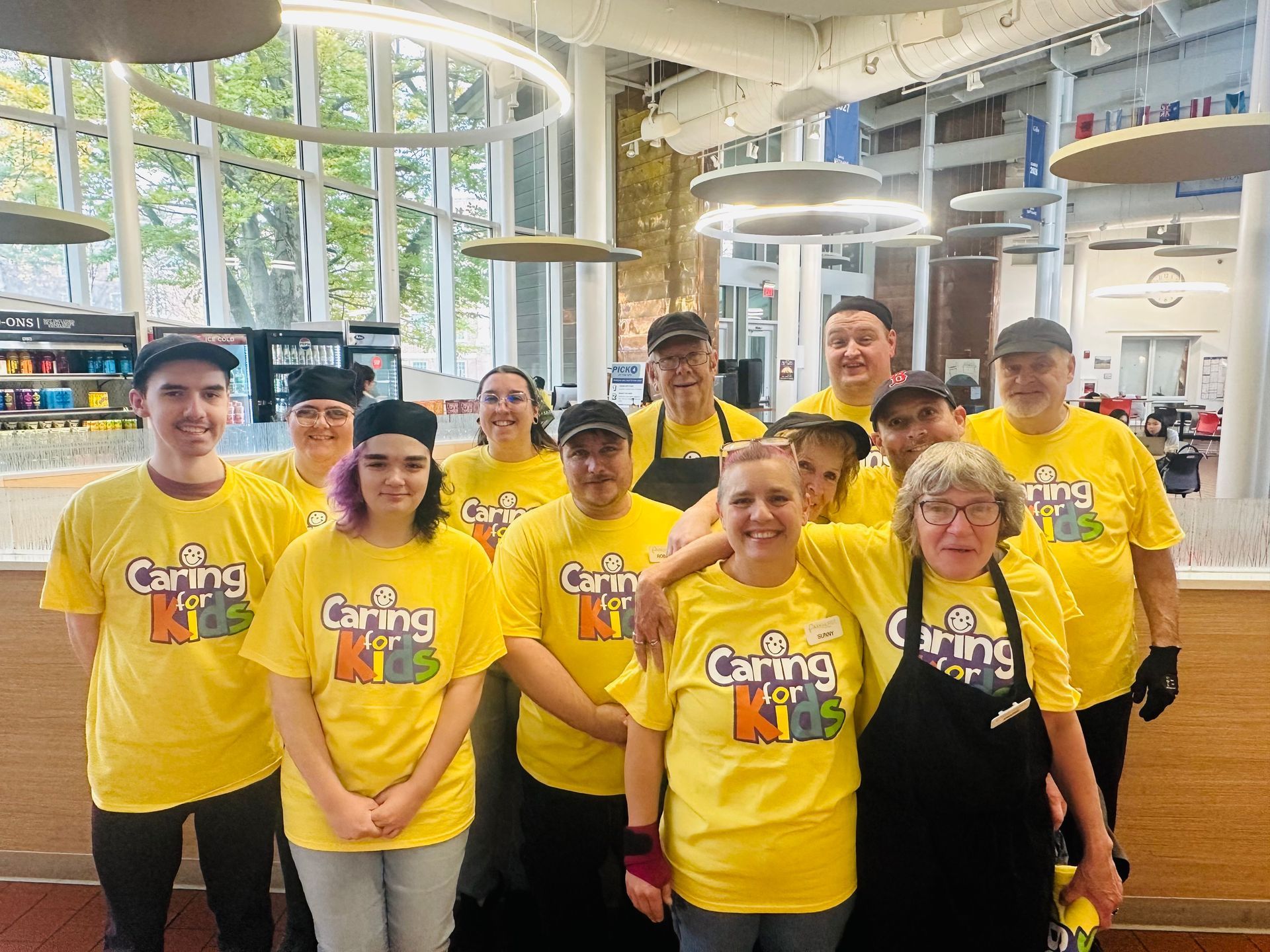 Group of people posing inside a shop with food products on shelves. Some hold food or drink, smiling.