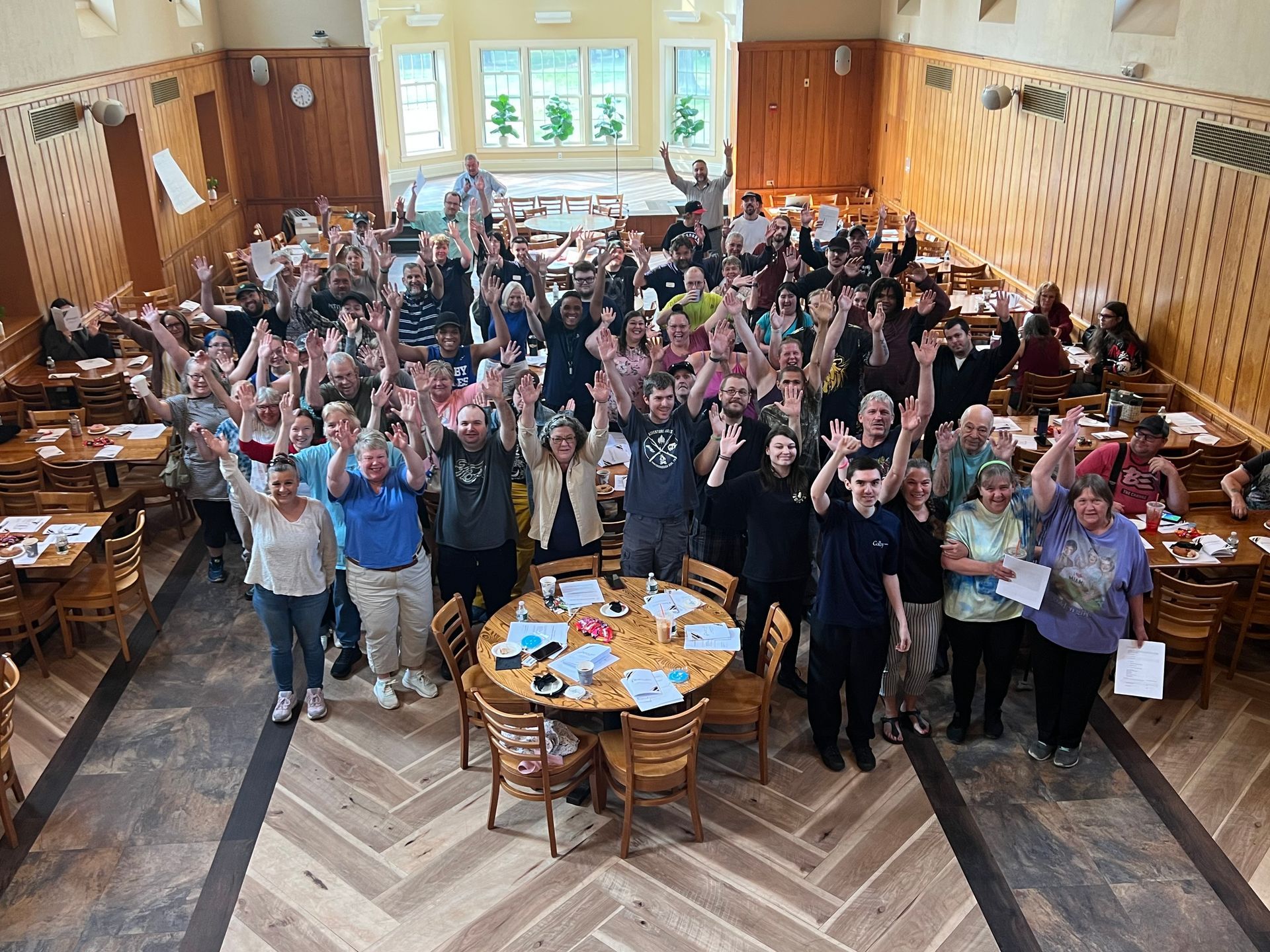 A group of people holding a large check in a brightly lit dining hall lobby, smiling at the camera.