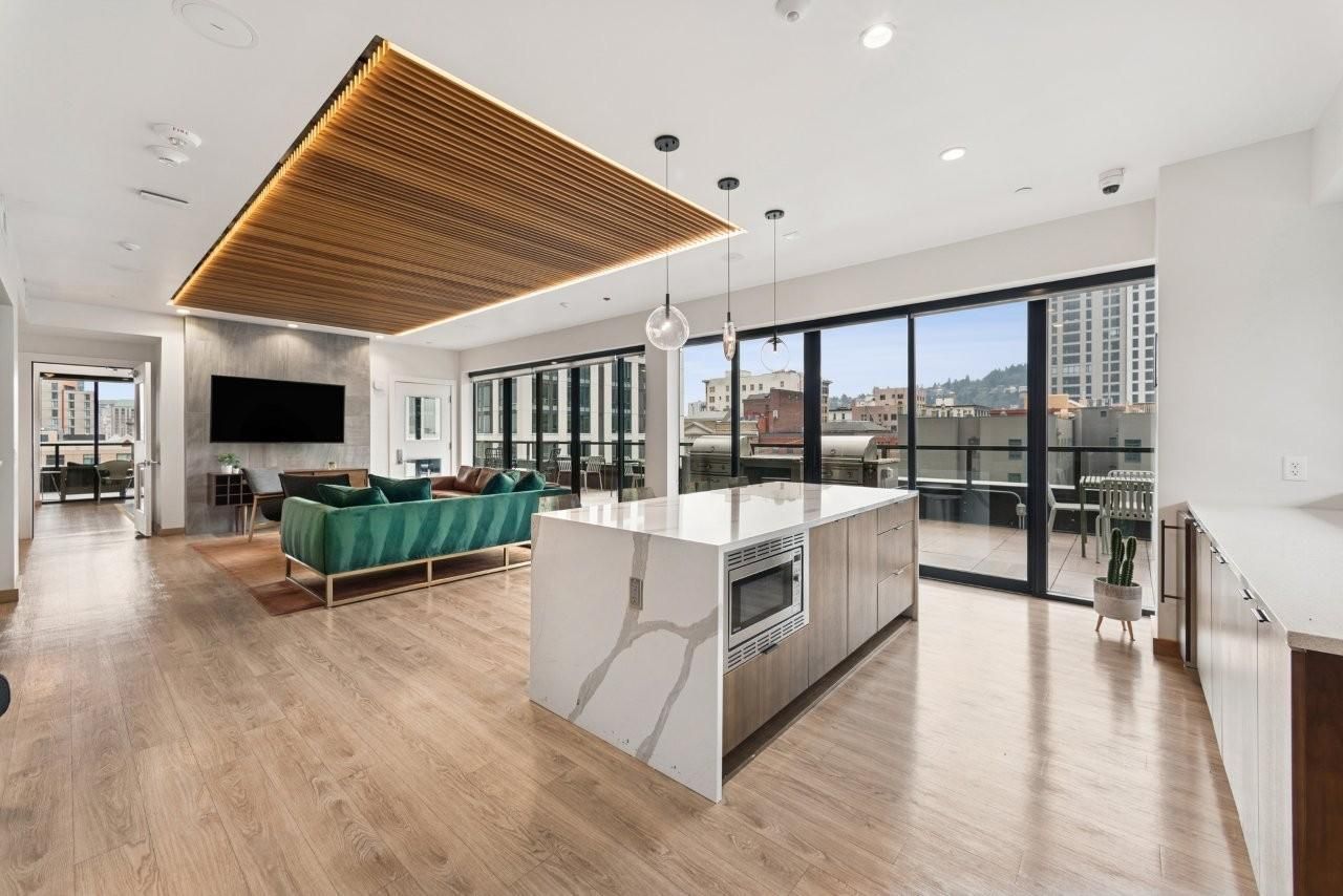 Modern open-concept living space with kitchen island, teal couch, and city view through sliding doors.