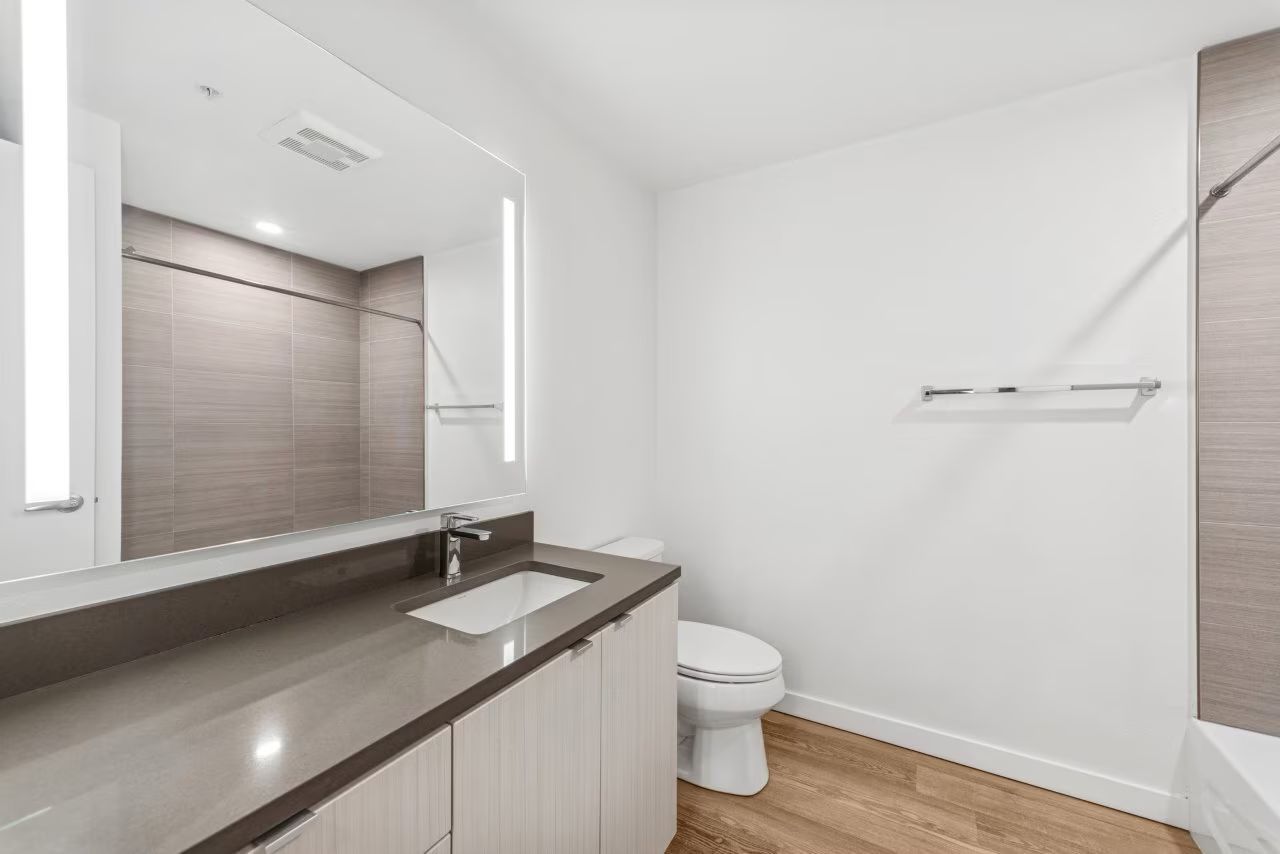 Modern bathroom with large mirror, gray countertop, white sink, and toilet.