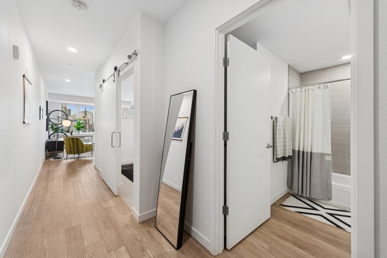 Long, white hallway with light wooden floors, a mirror, and an open bathroom doorway.