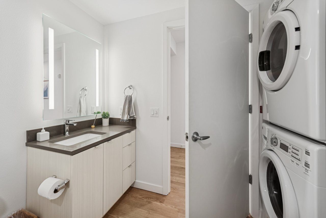 Bathroom with a sink, mirror, and stacked washer/dryer. Neutral color scheme, wood floor.