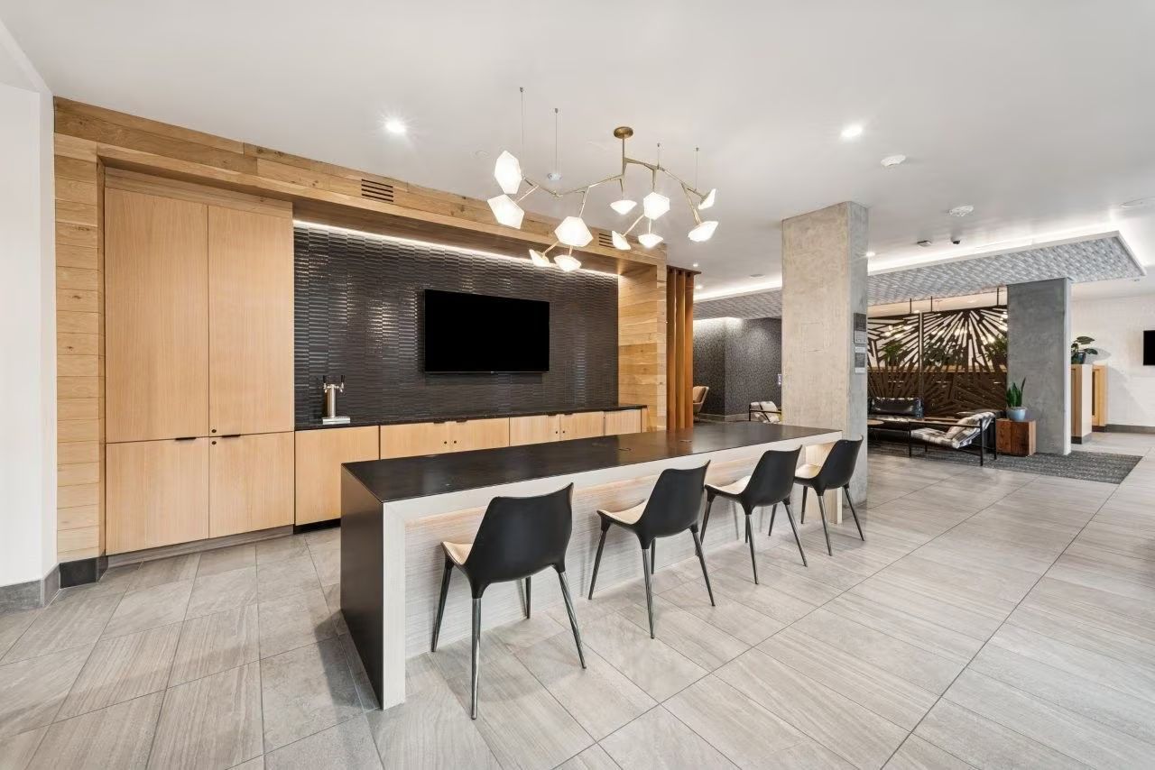 Modern lobby with a long counter and chairs, a TV, and decorative lighting.