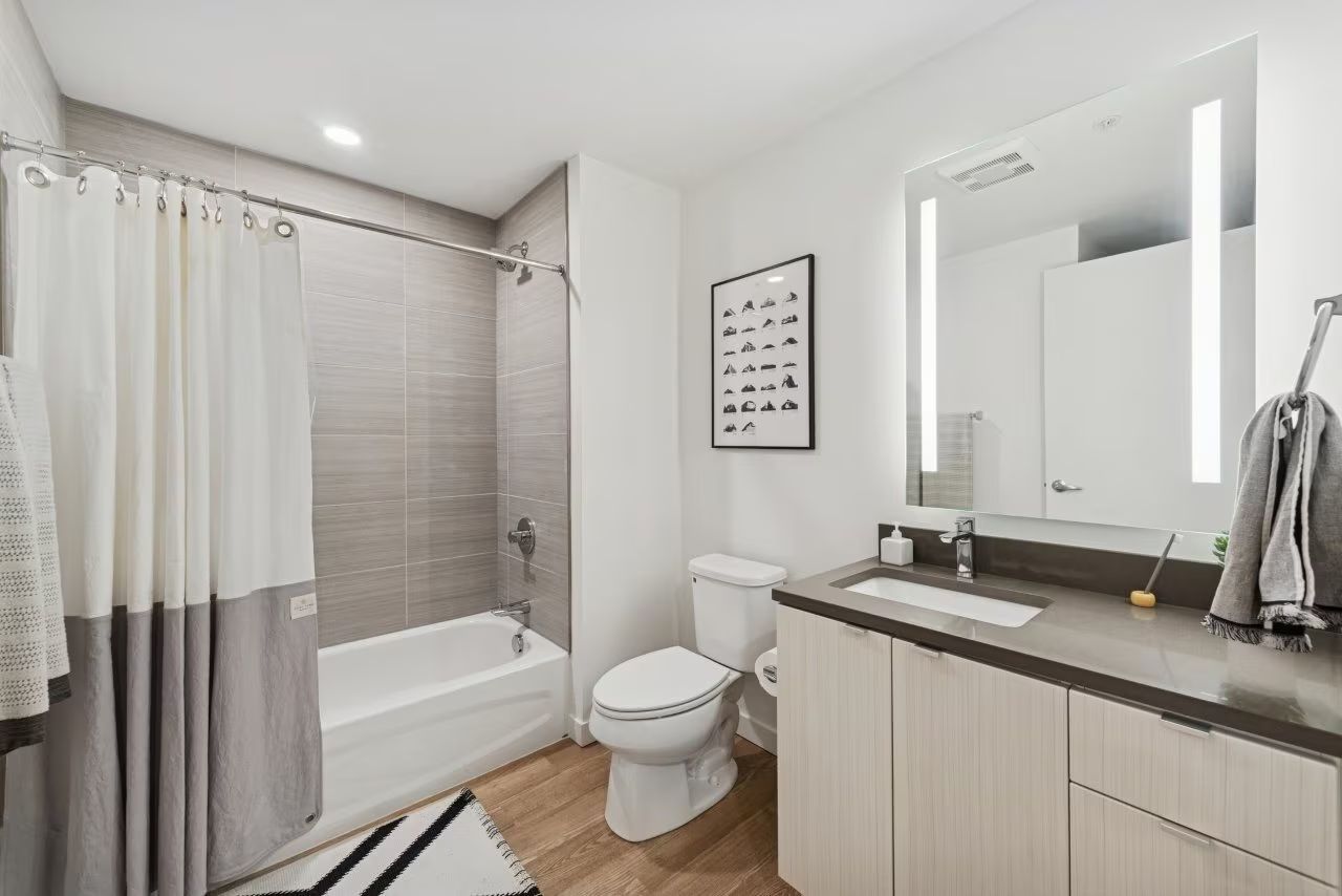 Modern bathroom with a bathtub, toilet, vanity, and a framed print on the wall. Light grey and white color scheme.