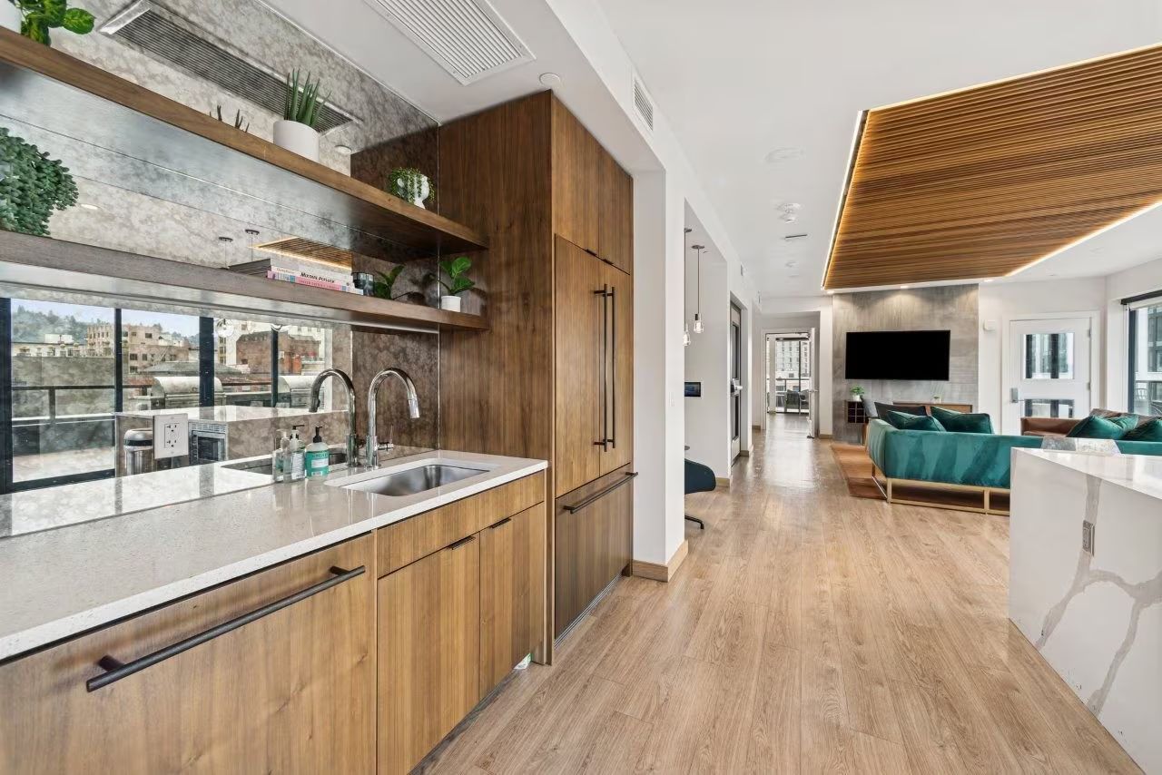 Modern kitchen and living space with wood cabinets, light wood flooring, and a long hallway.