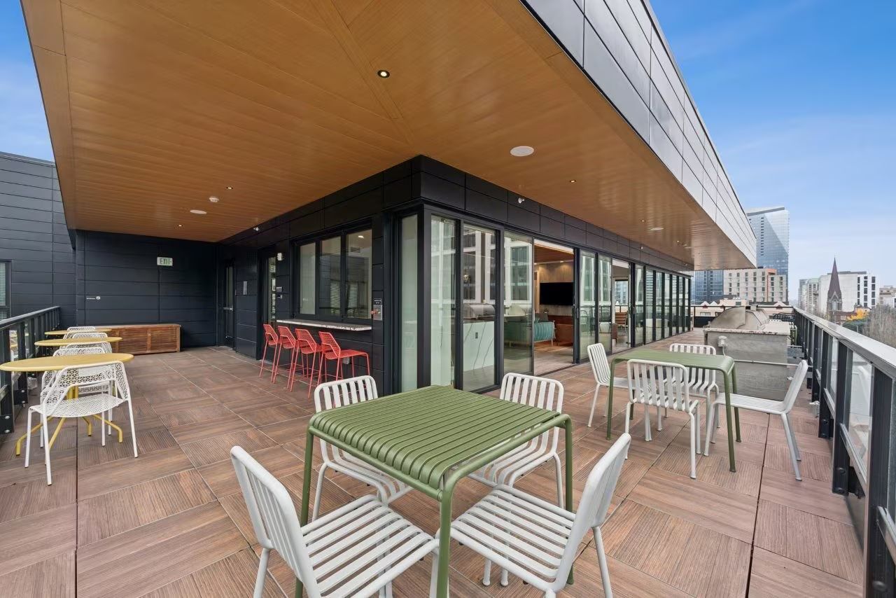 Outdoor patio with tables and chairs, adjacent to a modern building with a wood ceiling.