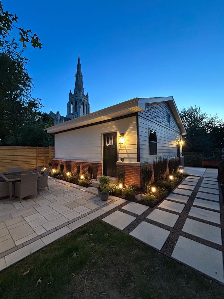 Rustic house patio at sunset with people seated outdoors, warm lights, and blooming trees in the yard
