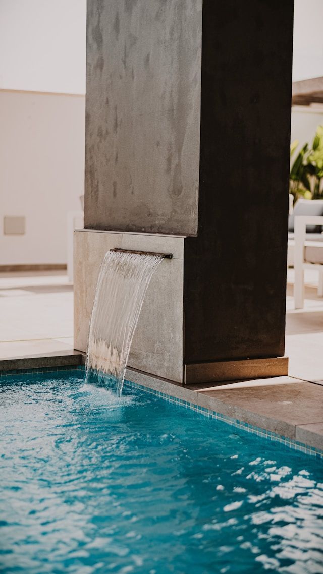 Poolside water feature spilling into a turquoise swimming pool