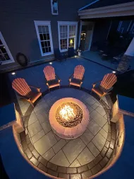 Nighttime backyard fire pit with four wooden chairs arranged around a glowing center.