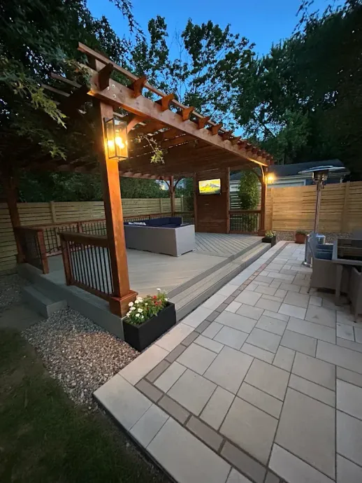 Backyard patio with pergola, warm lantern, and tiled seating area at dusk