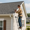 Worker on a ladder using a drill to repair the roof edge of a house