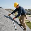 Worker in a yellow hard hat measuring a shingle roof with a tape measure.