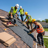 Roofing crew installing shingles on a sloped roof with tools and materials nearby