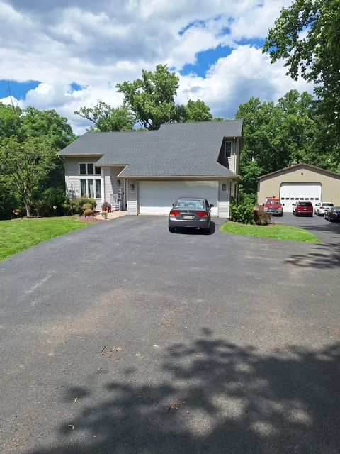 Suburban home with a long driveway, parked car, and detached garage under a partly cloudy sky