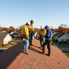 Workers in safety gear standing on a shingled roof in a residential neighborhood