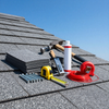 Roofing tools and materials on a shingled roof under a blue sky.