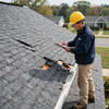 Inspector in yellow hard hat checking damaged roof shingles with a clipboard