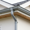 Gray gutter downspout at a house roof corner with soffit and fascia boards