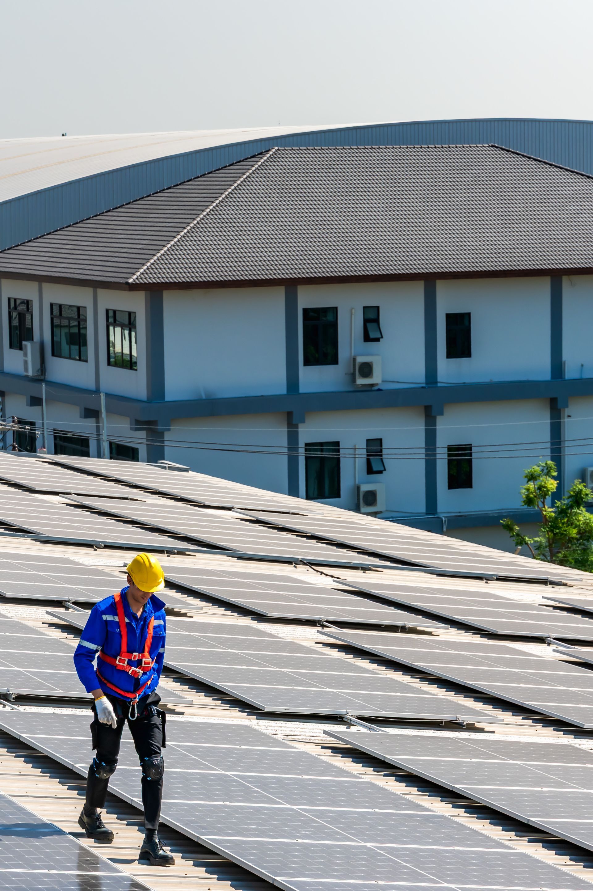 Worker in yellow hard hat and blue safety vest on a solar panel rooftop, with buildings in the background